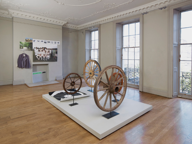 A Circle, image: foreground:  Rupert Ackroyd + David Gates 'Cart Wheel Exercise' 2014, a group of 5 works as follows: (i) 112 cm dia, oak, elm, steel on steel base, (ii) 70 cm dia, perspex, oak, ash, elm, paint, steel on steel base, (iii) 111 cm dia, pine, chestnut, steel on steel base, (iv) 60 cm dia, pine, steel on steel base, (v) 106 × 120 cm, unique photogram on paper, base: 200 × 300 cm, mdf, pine, paint; background left: International Lawns w. Vivien Lee 'A Fustian Proposal (slate grey corduroy), A Fustian Proposal (natural calico)' both S 2014, International Lawns w. Alex Mckellar 'RCA logotype test in colour 1 (team)' Epson Ultrachrome on 600gsm Somerset 104 × 139 cm 2014, 'RCA logotype test in colour 2 (entrance)' as previous 45 × 60 cm 2014, 'RCA logotype test in colour 3 (process)' as previous 23 × 34 cm 2014, International Lawns 'RCA logo proposal 2,3,6,14,19,23,24,31 photocopy, gouache, paper 19.5 × 19.5 cm 2014, International Lawns 'Sign' screen print on cutting mat 58.5 × 92 cm 2014; installation photography by Andy Keate